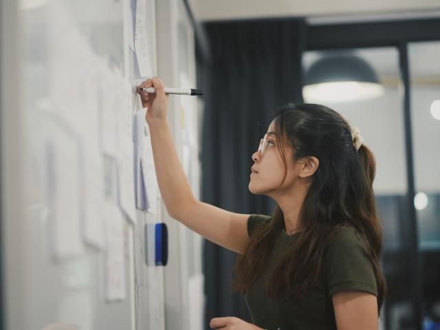 A person drawing on a white board with papers stuck to it